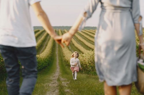 A family holds hands with their child in a beautiful, green field under a clear sky.