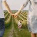 A family holds hands with their child in a beautiful, green field under a clear sky.
